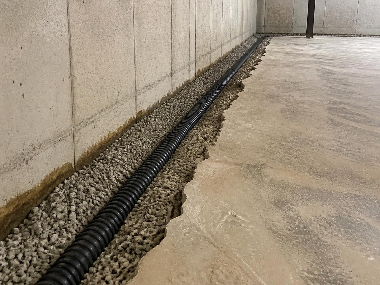 Interior perimeter drain tile bedded in washed gravel in a trench cut along a basement foundation wall