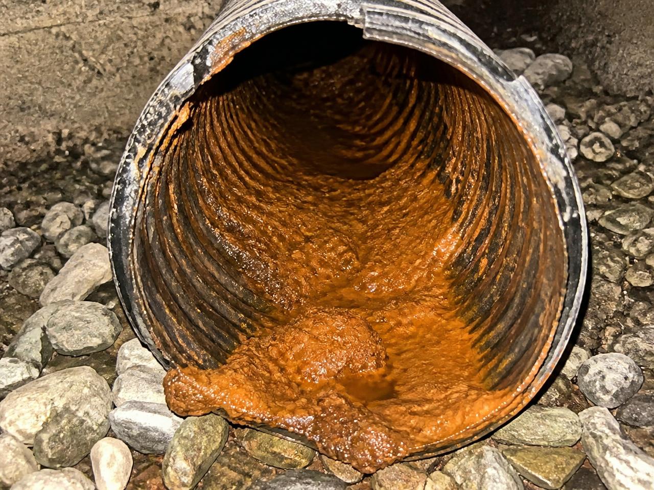 Interior of a basement drain tile pipe coated with thick orange-brown iron ochre deposits